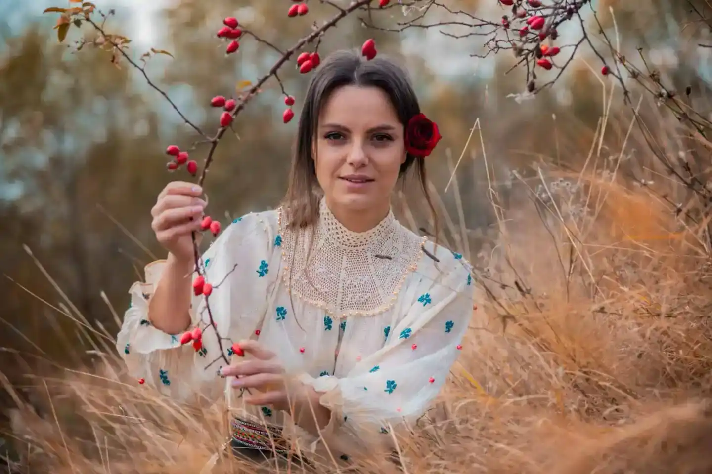 Junge Frau in traditionellem Leinenkleid mit Stickerei hält Rosenblüten-Zweig, Portrait Wien in herbstlicher Natur