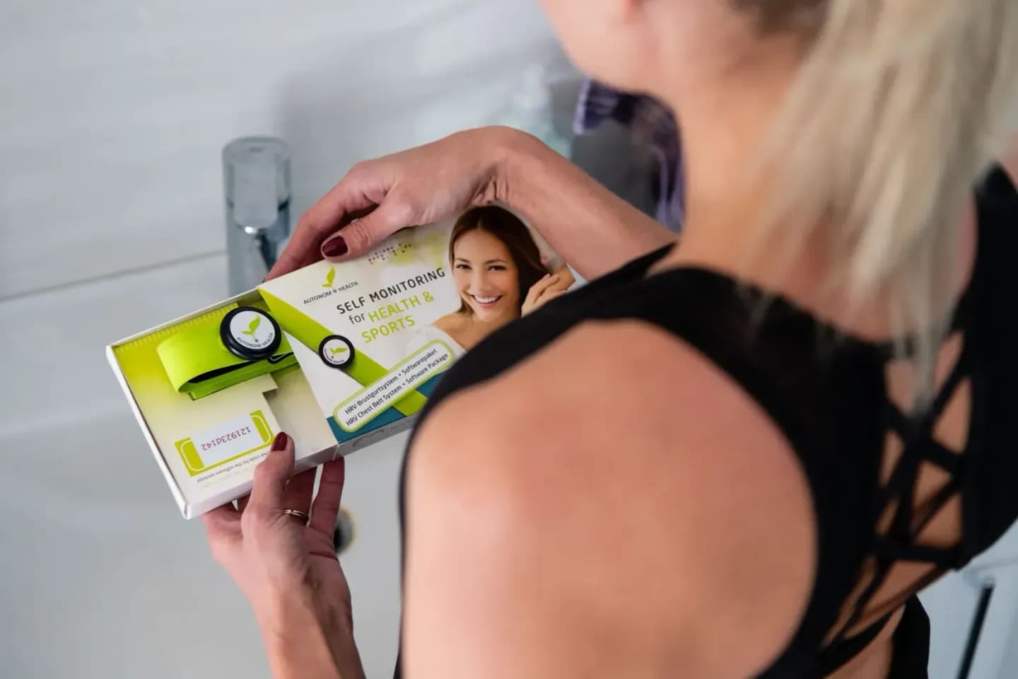 Frau hält Produktverpackung für Gesundheits- und Sportmonitoring in die Kamera, professionelle Produktfotografie Wien