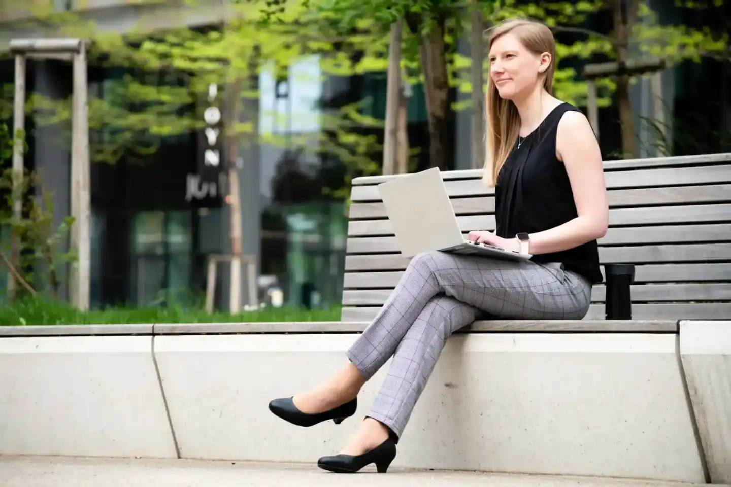 Junge Frau mit Laptop sitzt auf einer Bank in urbaner Umgebung – Corporate Fotografie Wien