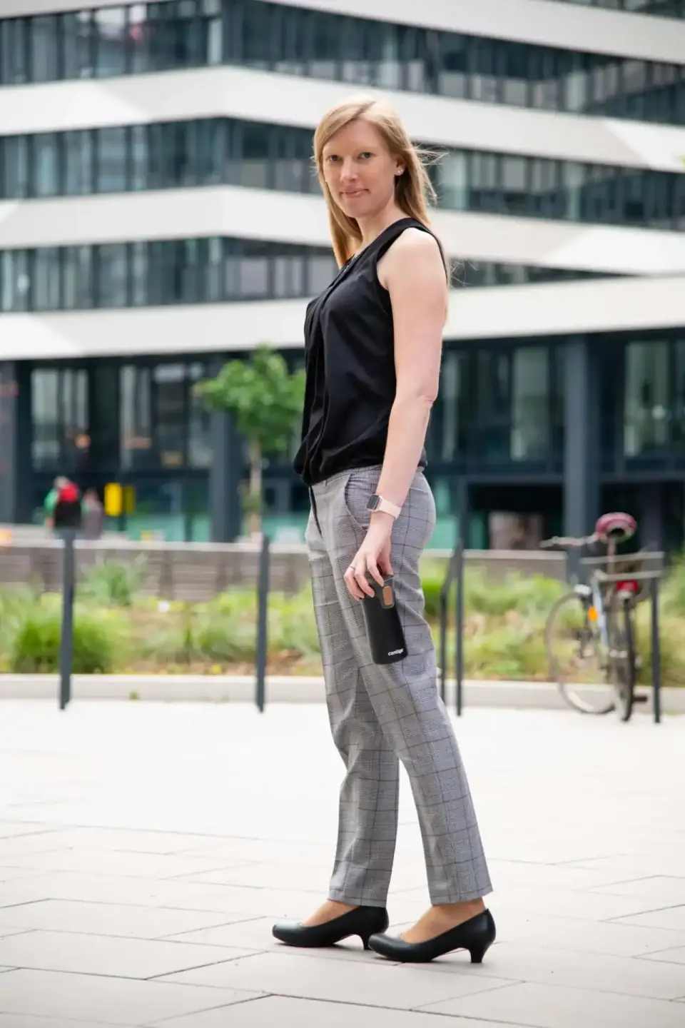 Geschäftsfrau in schwarzem Oberteil und karierter Hose steht vor modernem Gebäude – professionelles Headshot eines Business F