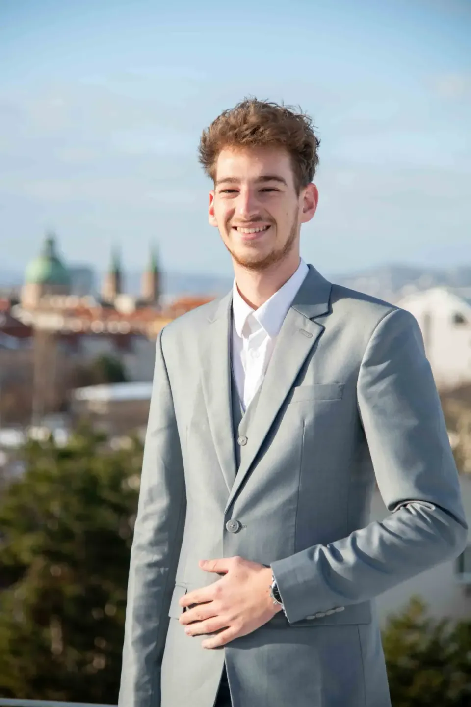 Junger Mann im grauen Anzug lächelt vor Wiener Stadtpanorama - Business Fotografie Wien