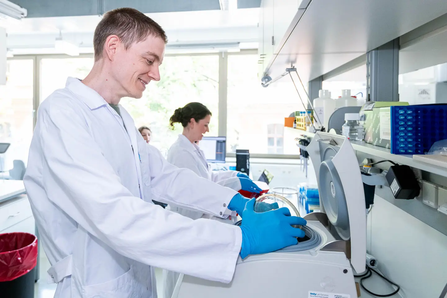 Laechelnder Laborant an der Zentrifuge im Biotech-Labor, Business Fotograf Wien