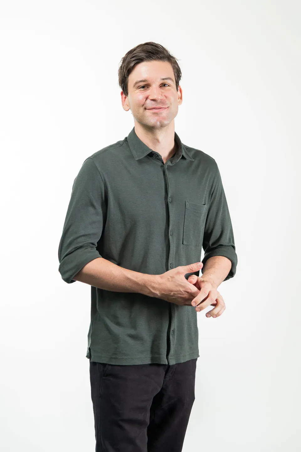 Mann mit gefalteten Haenden und sanftem Laecheln im Corporate Headshot, Wien