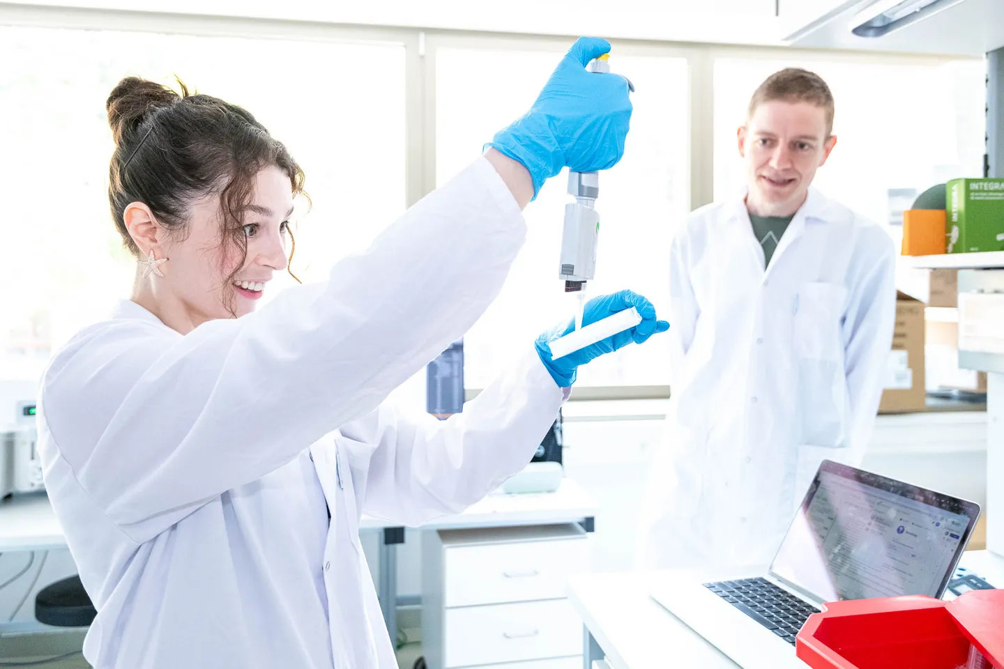 Lachende Laborantin beim Pipettieren im Biotech-Labor, Mitarbeiterfotos Wien