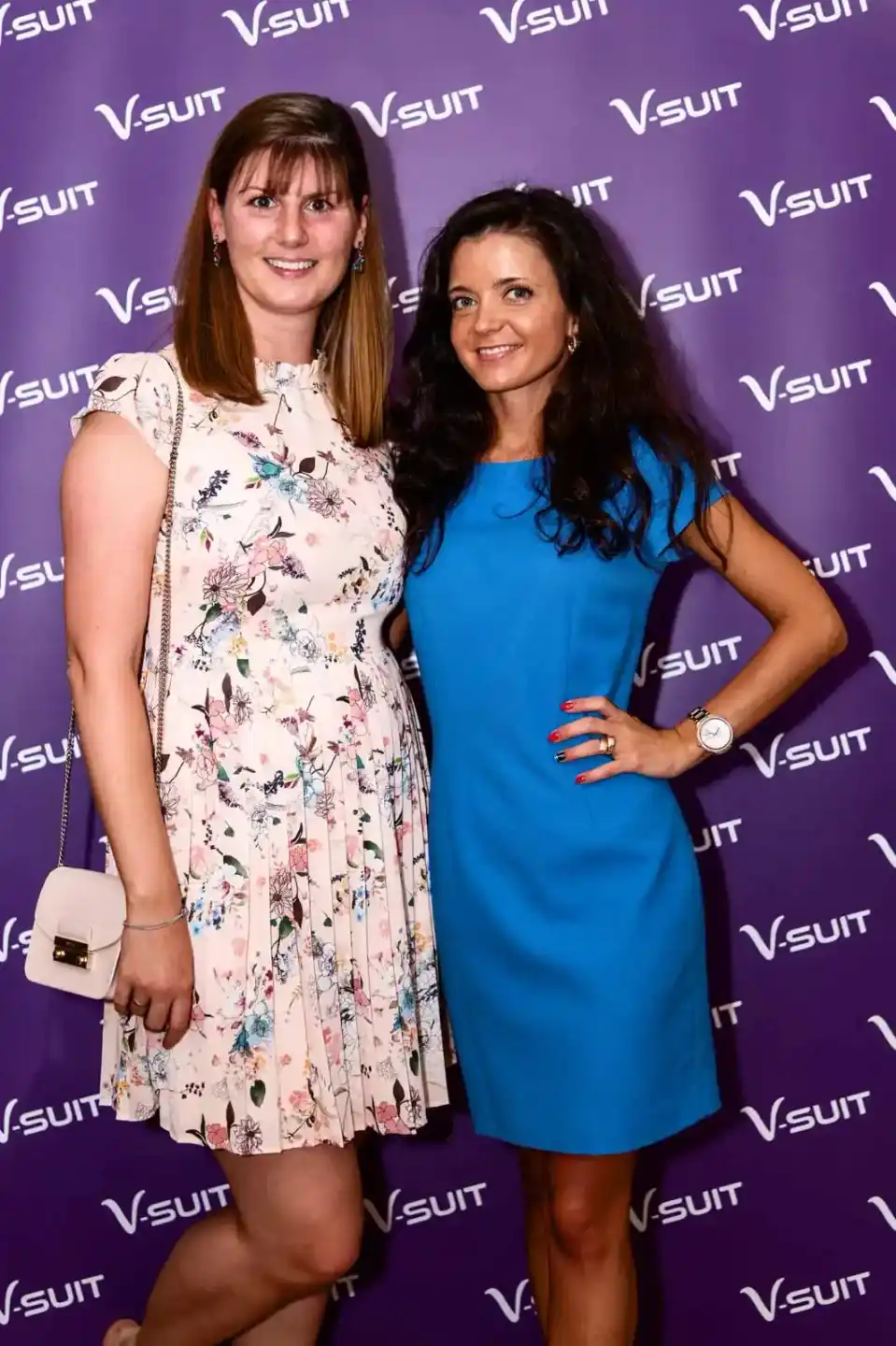 Zwei Frauen posieren vor lila Hintergrund mit V-SUIT Logo bei einem Eventfotografie Wien Event