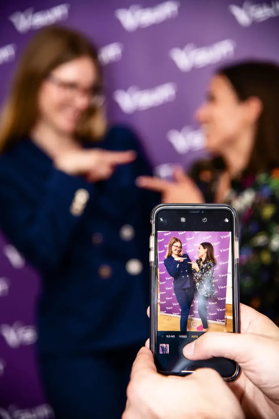 Eventfotograf dokumentiert zwei Frauen beim Interview vor lila Hintergrund mit Branding