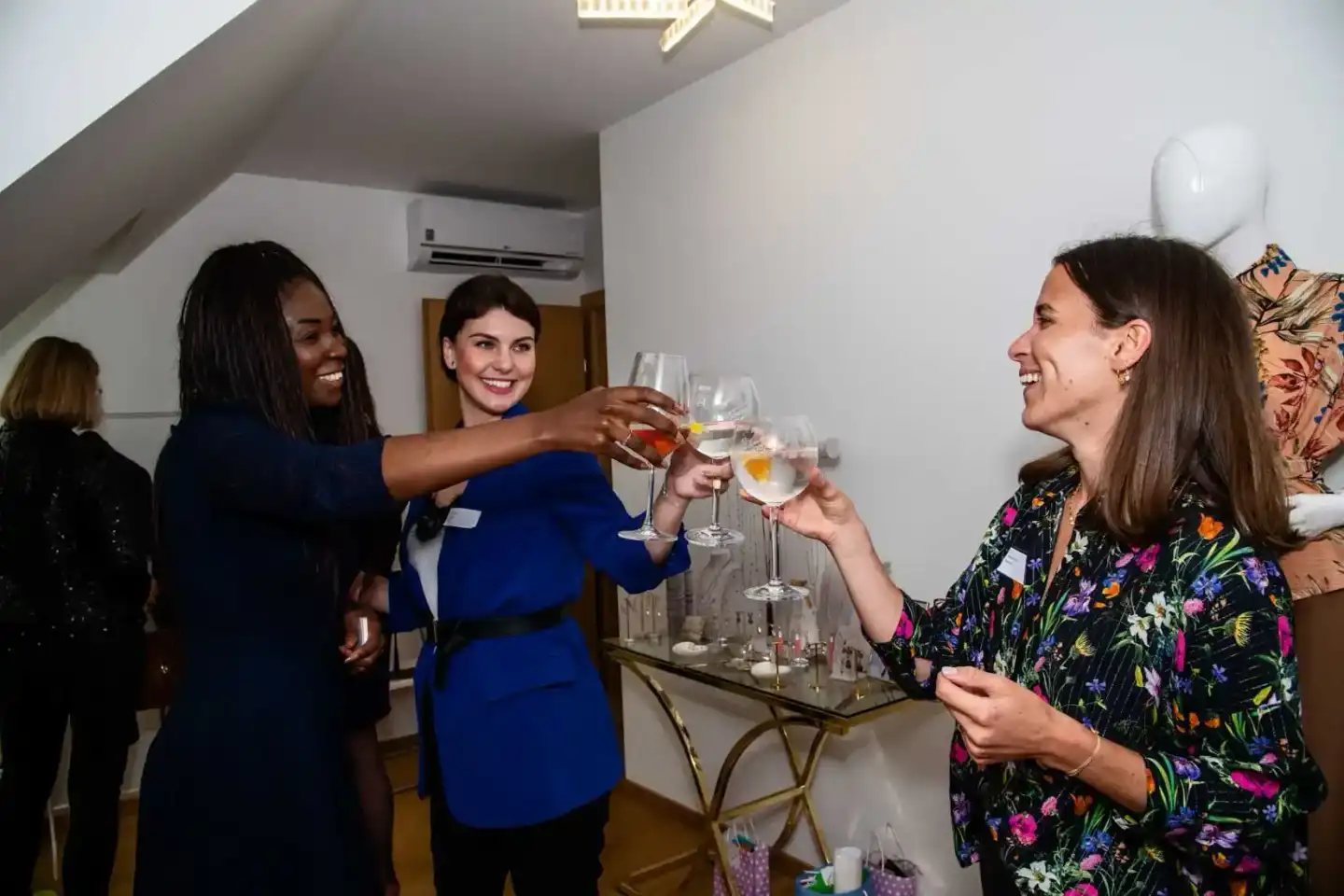 Drei Frauen stoßen mit Cocktails an einem Firmenevent in Wien an und lachen zusammen