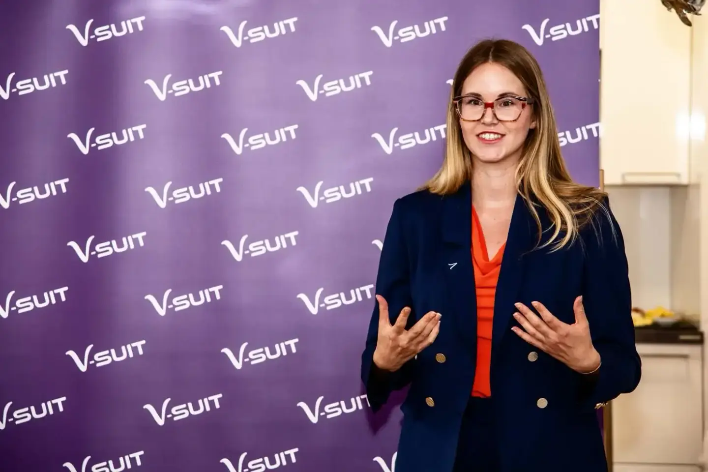 Frau mit Brille und rotem Oberteil vor VSUIT-Backdrop bei Eventfotografie Wien