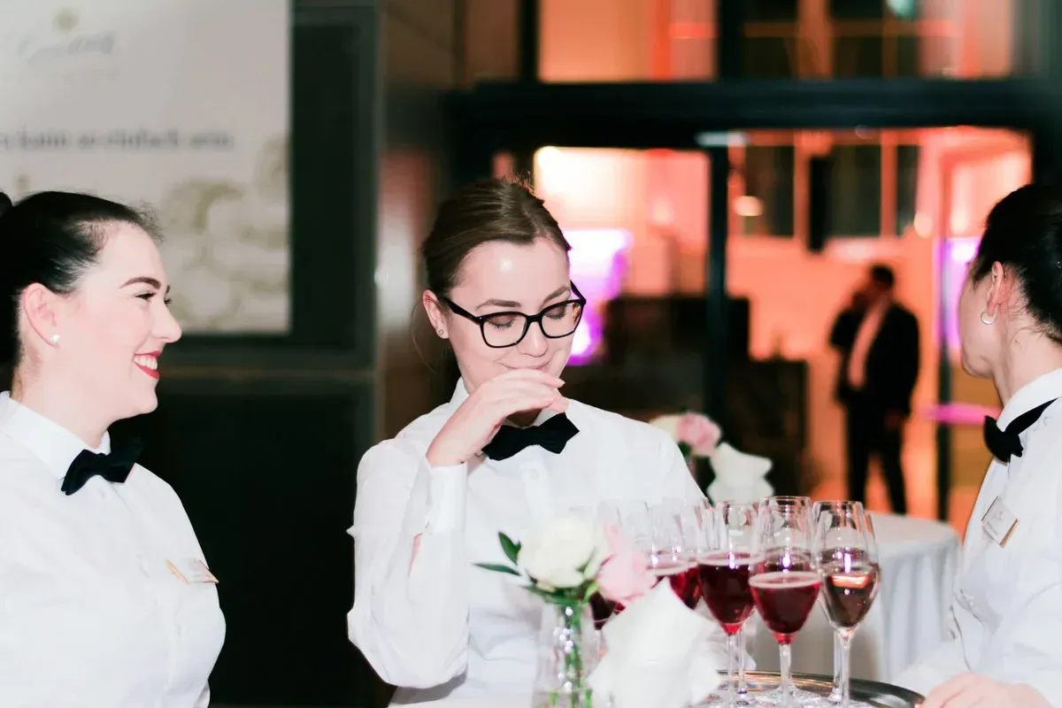 Drei elegant gekleidete Personen in weißen Hemden mit Fliegen unterhalten sich bei einem Firmenevent in der Hofburg Wien, im 