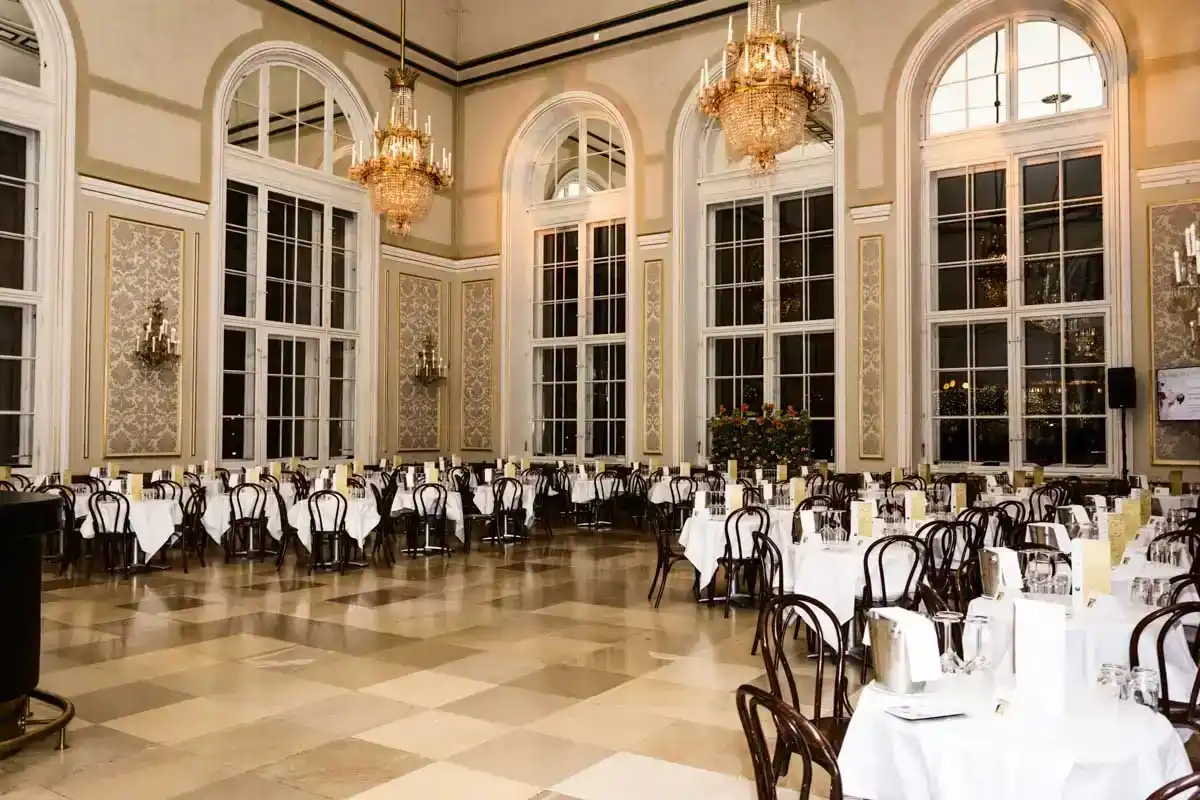 Eleganter Veranstaltungssaal in der Hofburg Wien mit weißgedeckten Tischen, schwarzen Stühlen und kristallklaren Kronleuchter