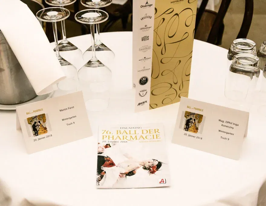 Elegante Tischeindeckung beim 76. Ball der Pharmacie in der Hofburg mit Sektgläsern, Platzkarten und Programm - professionell