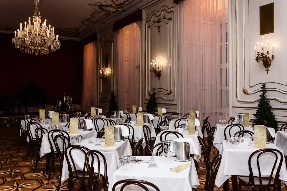 Eleganter Ballsaal in der Hofburg Wien mit weißgedeckten Rundtischen, Bentwood-Stühlen und Kristalllüstern - professionelle E
