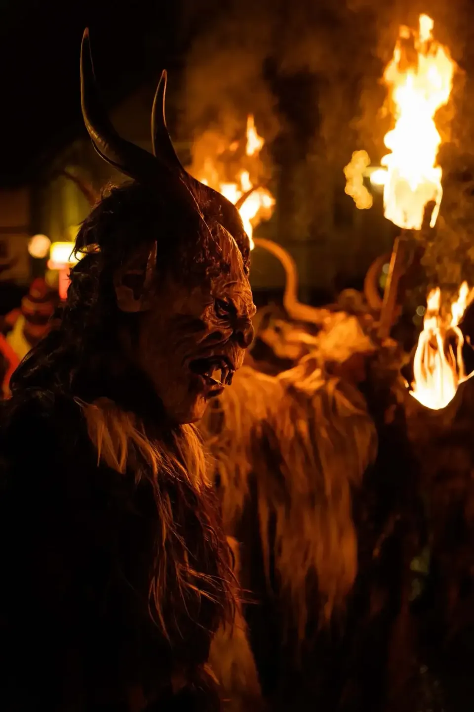Krampus-Figur mit Hörnern und Maske bei Nacht vor loderndem Feuer, professionelle Eventfotografie Wien