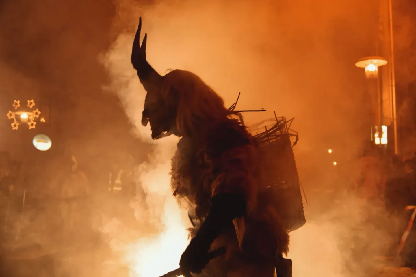 Krampus-Figur in dramatischer Pose mit Hörnern und Fell vor orangem Feuer und Rauch, professionelle Eventfotografie Wien