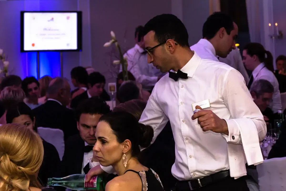 Eventfotograf Wien dokumentiert elegante Gala: Mann in weißem Hemd und Fliege spricht mit Gästen in festlicher Atmosphäre mit