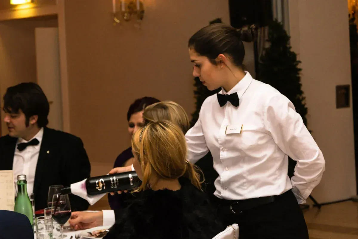Serviererin in weißem Hemd und schwarzer Schürze schenkt Wein bei eleganter Veranstaltung im Kursalon Wien ein