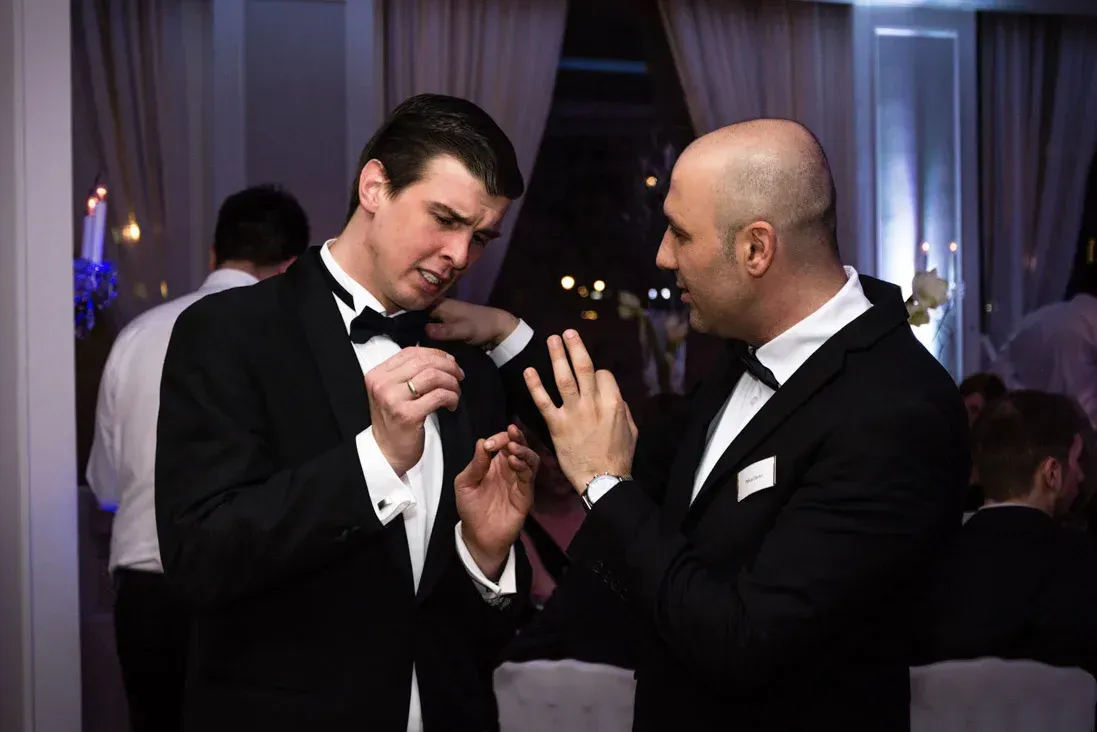 Zwei Männer im Smoking unterhalten sich auf einem Firmenevent Wien, im Hintergrund elegante Veranstaltungsräume mit Vorhängen