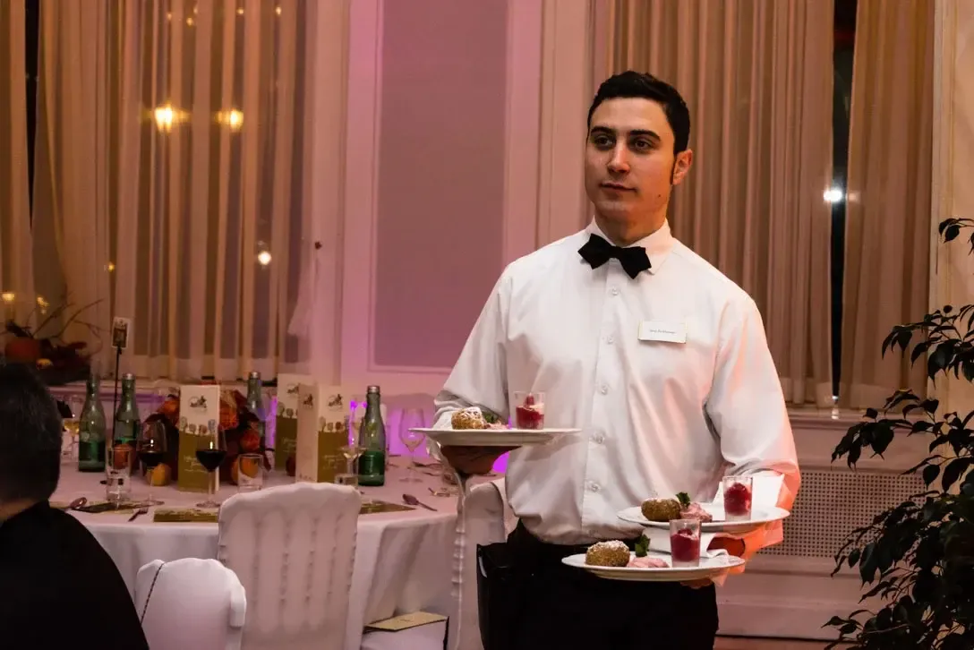 Kellner im weißen Hemd und schwarzer Fliege serviert Appetizer bei eleganter Veranstaltung im Kursalon Wien