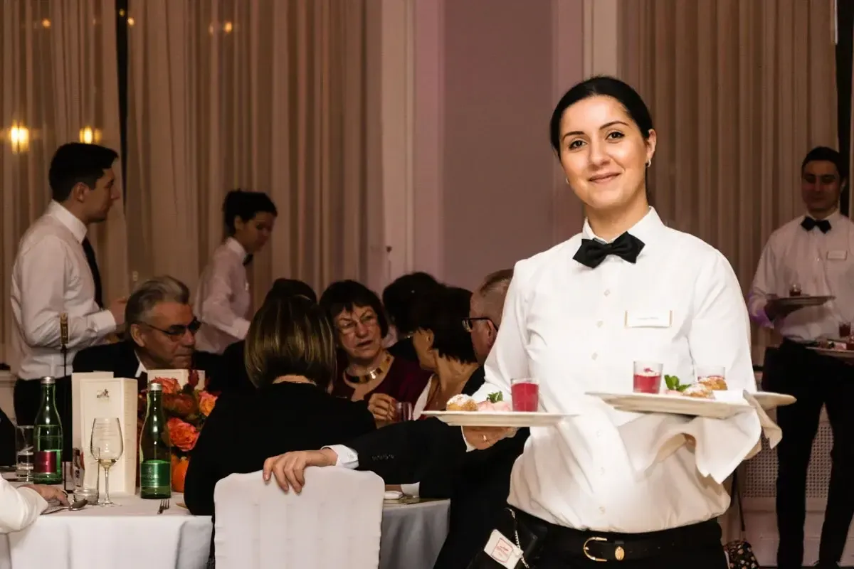 Kellnerin im weißen Hemd und schwarzer Fliege serviert Gästen im eleganten Saal – Eventfotografie Wien