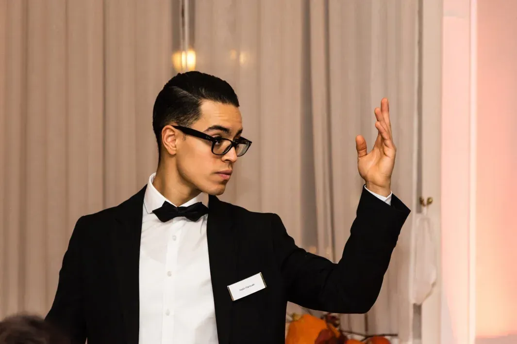 Eleganter Moderator im Smoking mit Brille bei Eventfotografie Wien, gestikulierend vor Vorhang