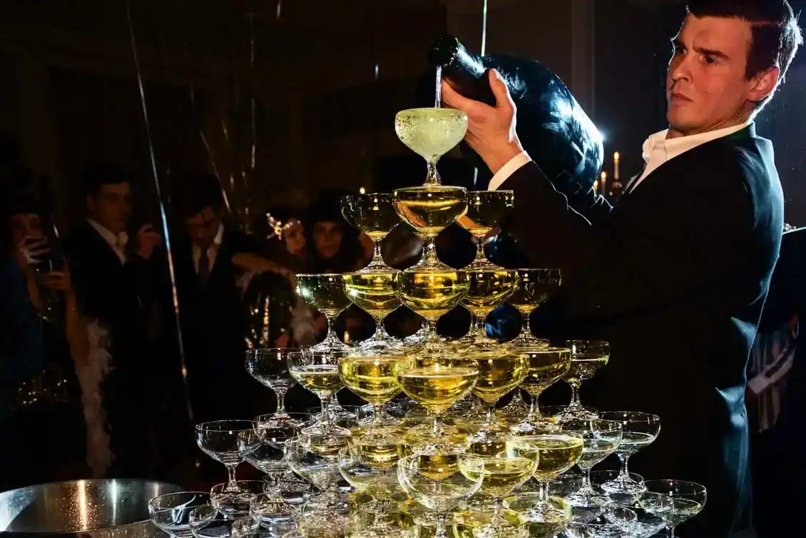 Eleganter Barkeeper präsentiert eine Champagner-Pyramide bei einem exklusiven Firmenevent Wien mit Gästen im Hintergrund