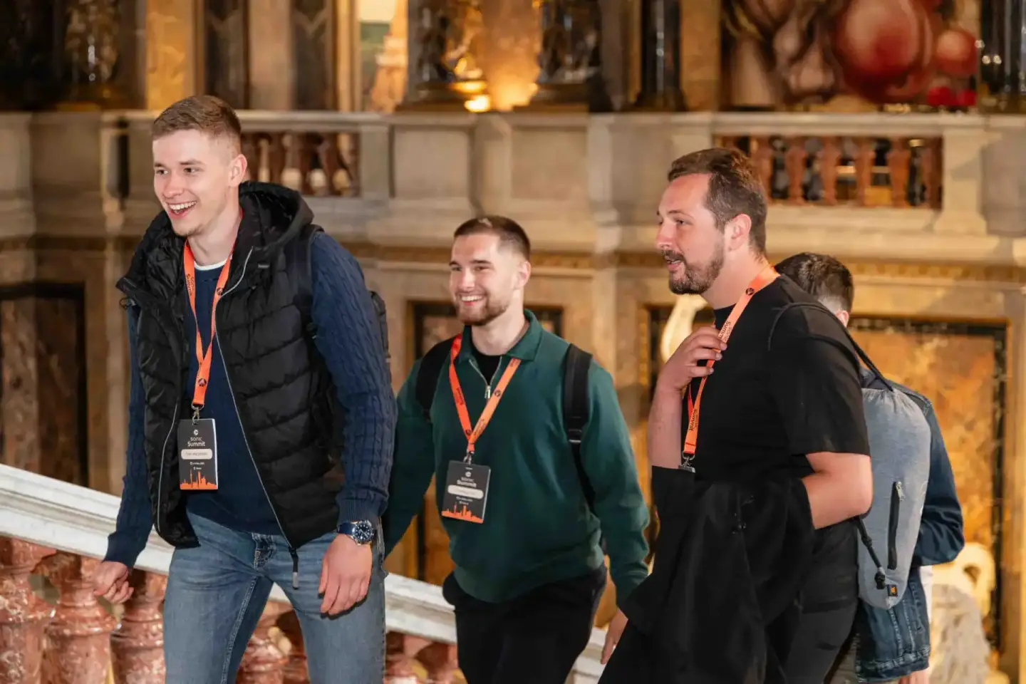 Vier Männer mit Event-Badges lachen zusammen vor einer beleuchteten Steinwand beim Sonic Summit – professionelle Eventfotogra