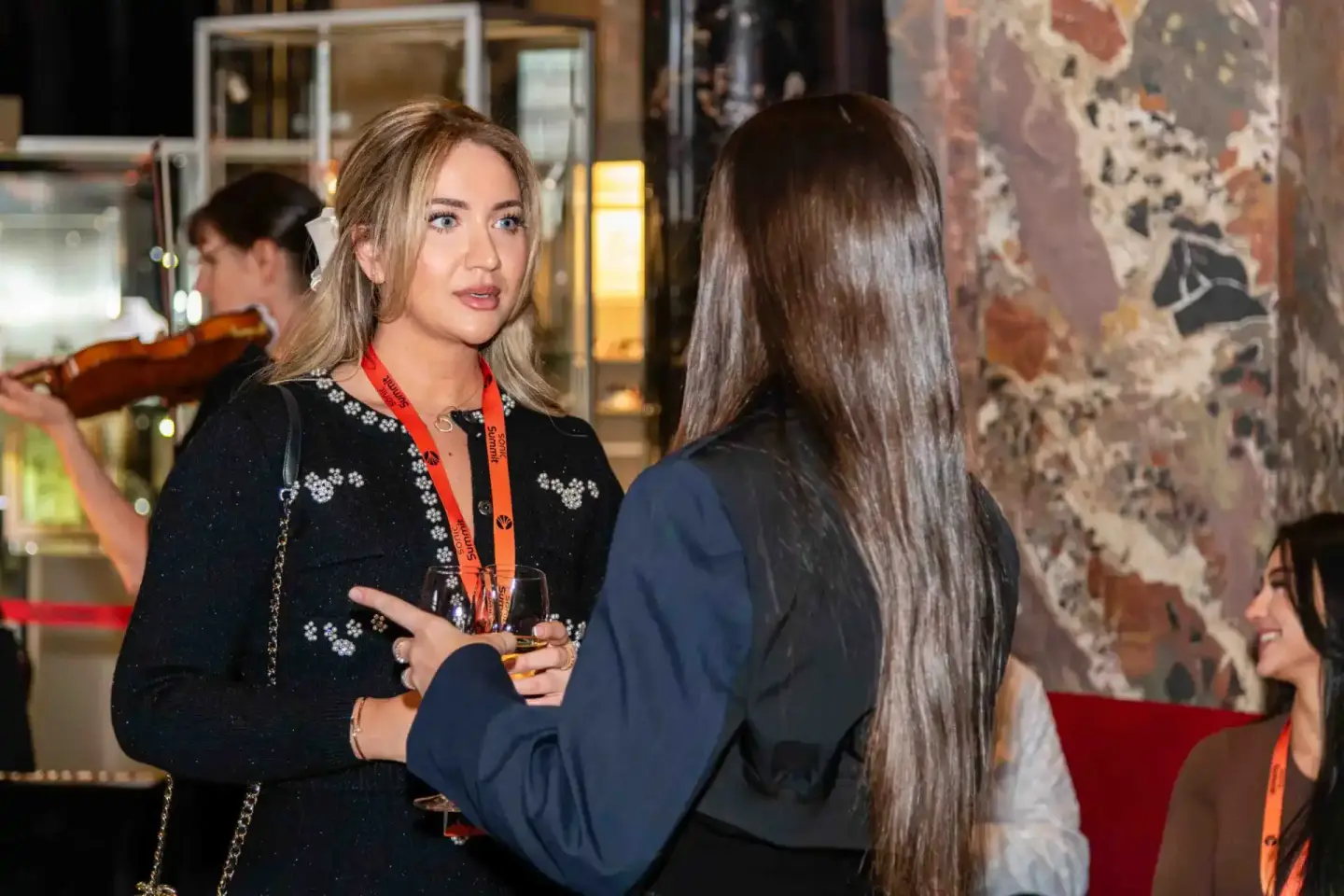 Zwei Frauen im Gespräch auf dem Sonic Summit Event in Wien, eine trägt schwarzes Blazer mit Stickerei und rote Lanyardkarte
