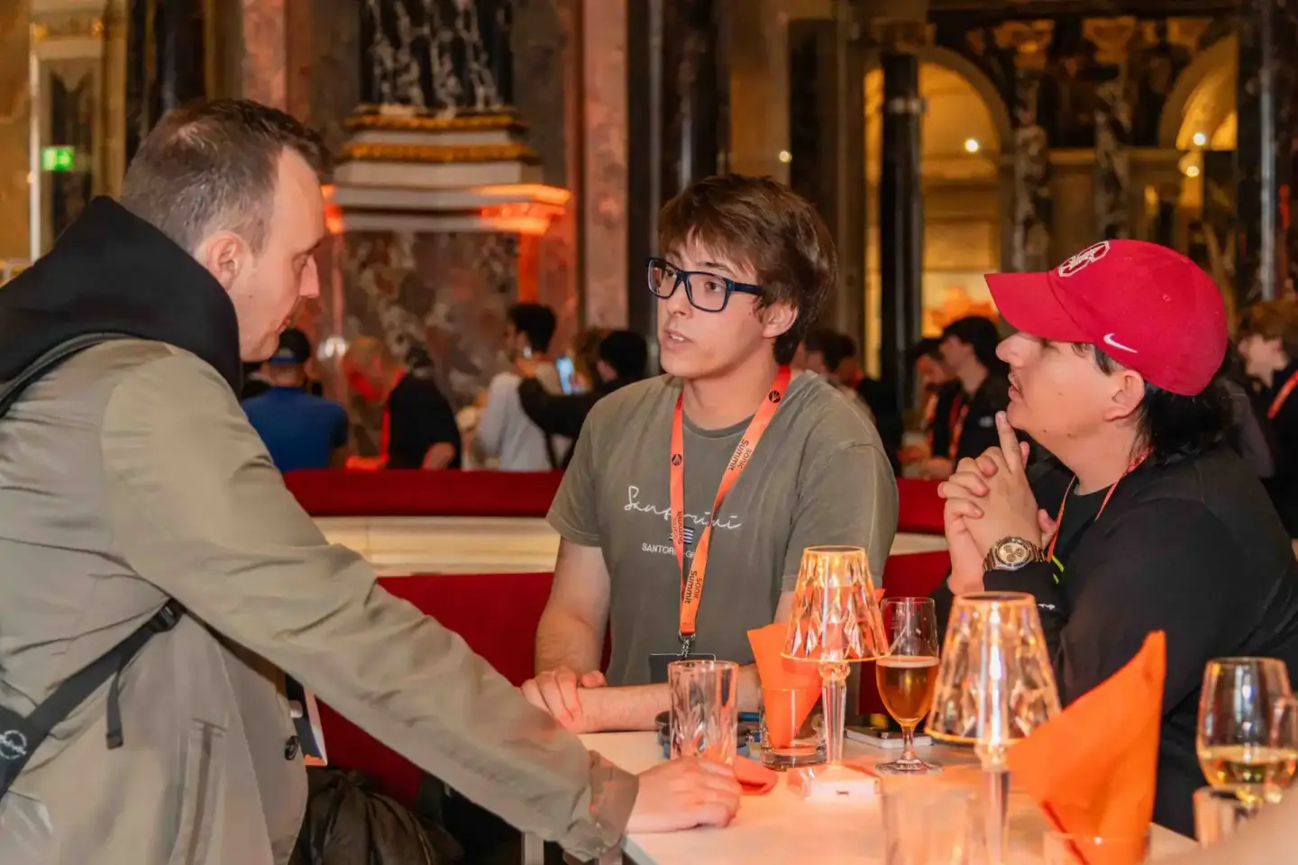 Drei Personen im Gespräch bei einem Firmenevent in Wien, einer trägt ein oranges Namensschild und eine Brille