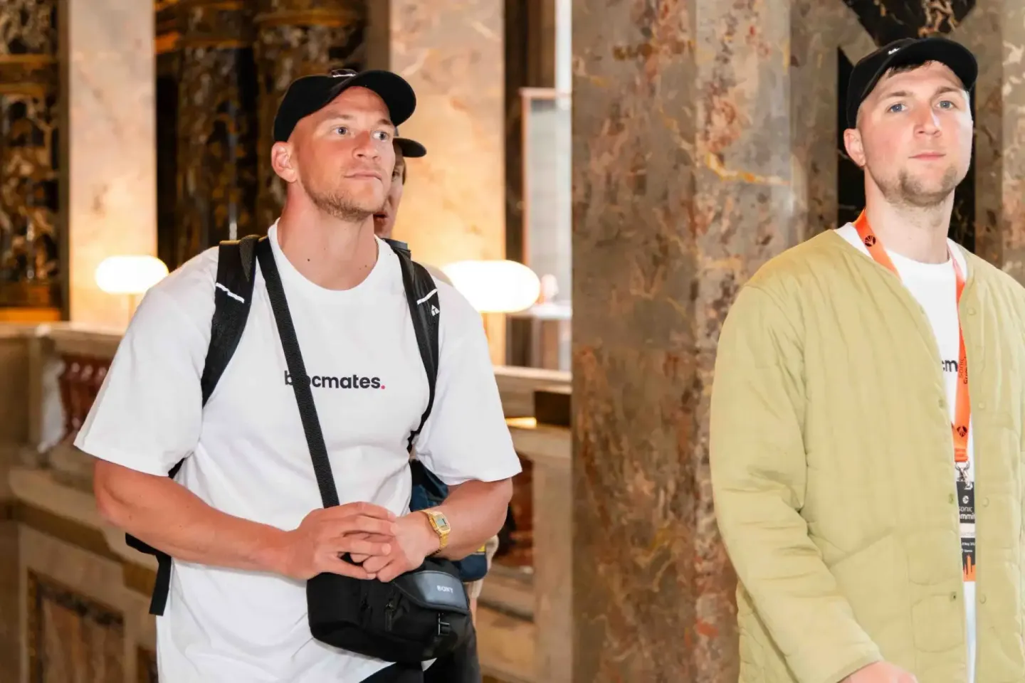 Zwei Besucher beim Sonic Summit Event in Wien, einer trägt ein weißes T-Shirt mit Rucksack, der andere ein gelbes Hemd mit La