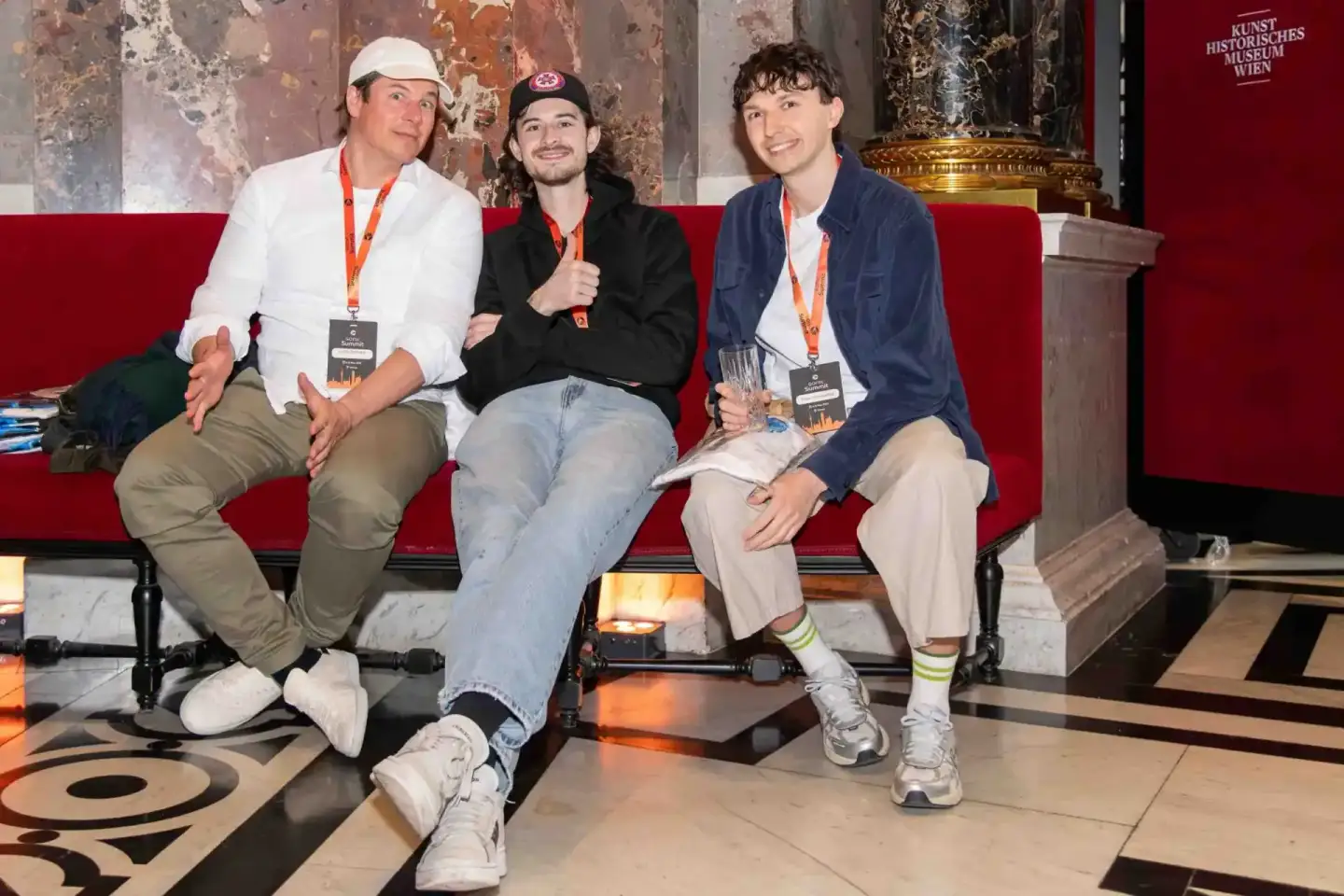 Drei junge Männer mit Lanyards sitzen auf rotem Sofa im Kunsthistorischen Museum Wien während eines Firmenevent