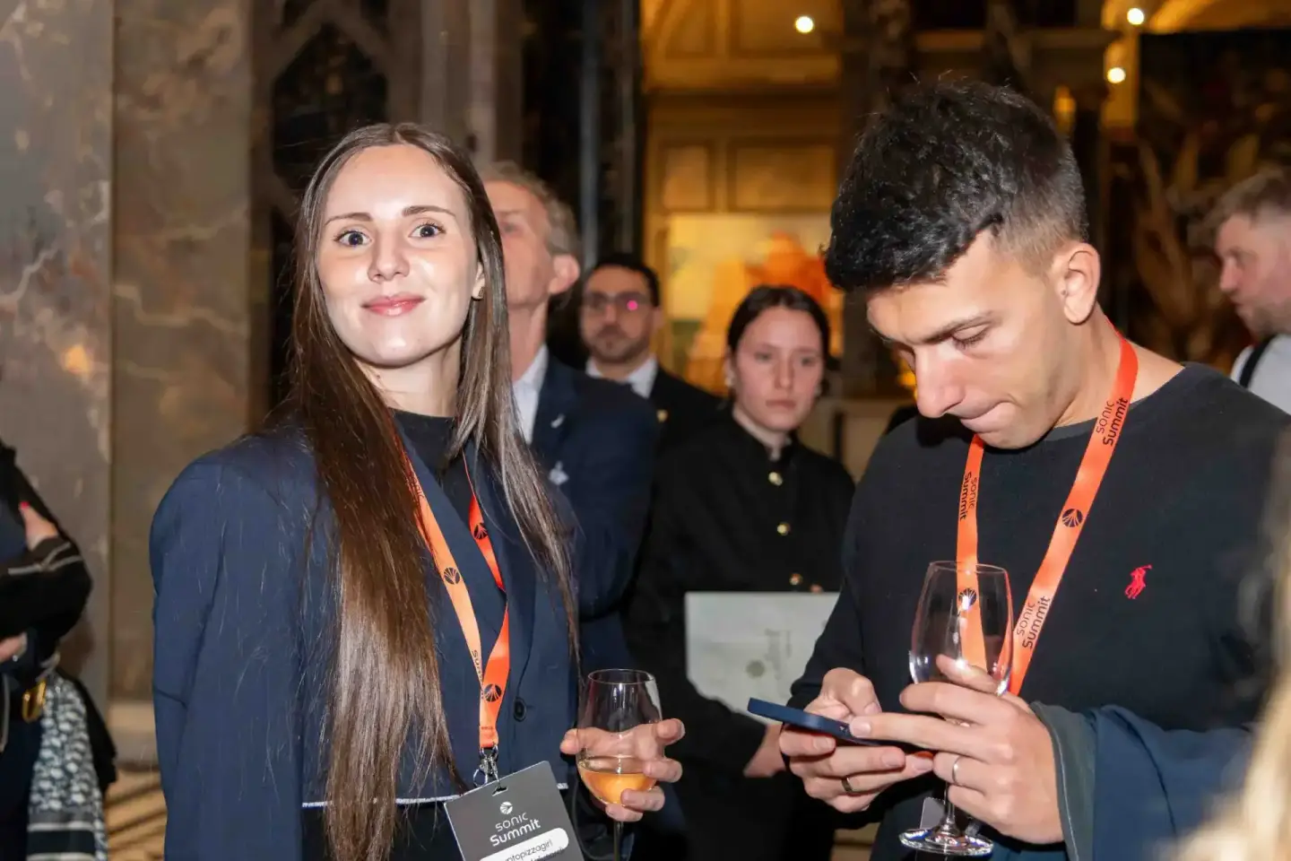 Zwei junge Profis mit orangenen Lanyards beim Sonic Summit Event in Wien, einer schaut auf sein Smartphone