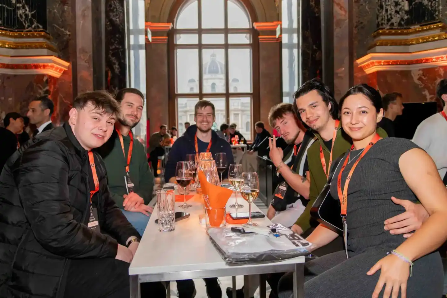 Gruppe von Teilnehmern beim Sonic Summit Event in Wien sitzt an einem Tisch mit Getränken, im Hintergrund große Fenster mit S