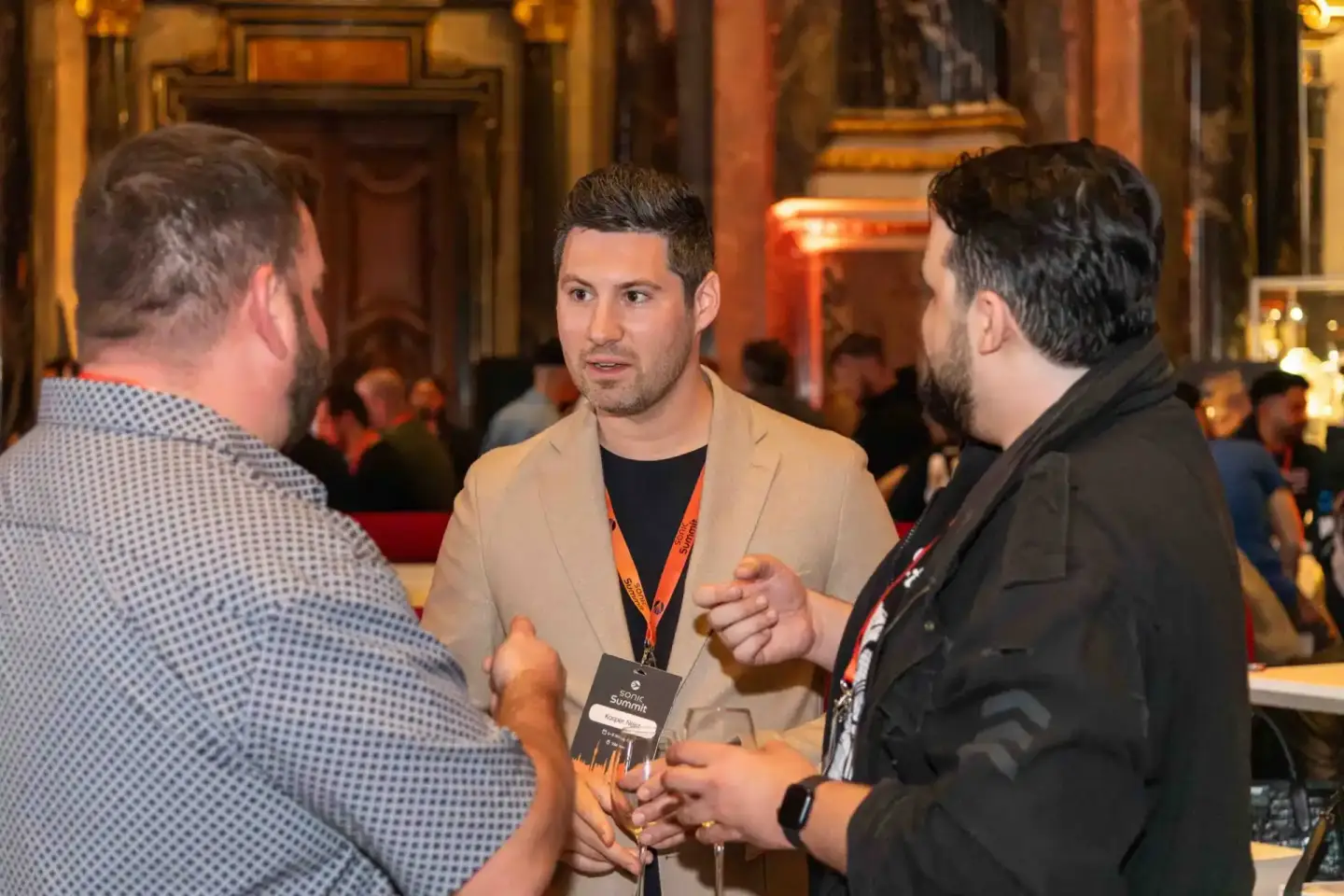 Drei Männer im Gespräch beim Sonic Summit Event in Wien, zwei tragen Ausweisbänder, elegante Veranstaltungsfotografie