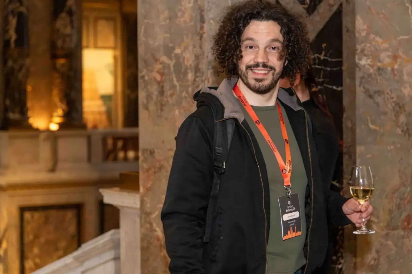 Lächelnder Mann mit Akkreditierungsausweis hält Weißweinglas beim Sonic Summit Event in Wien