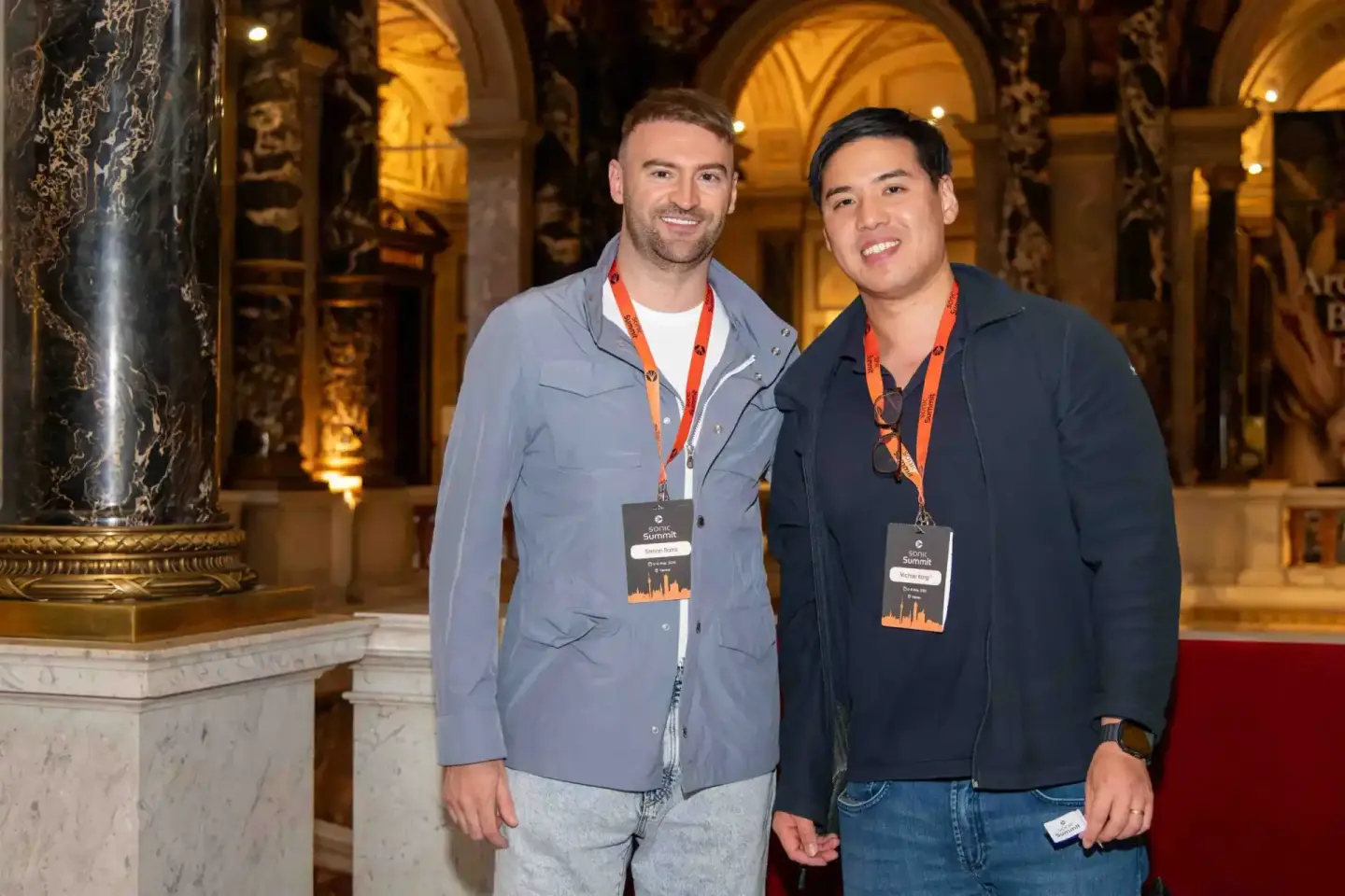 Zwei Teilnehmer beim Sonic Summit Event in Wien tragen Ausweisbänder vor historischer Architektur