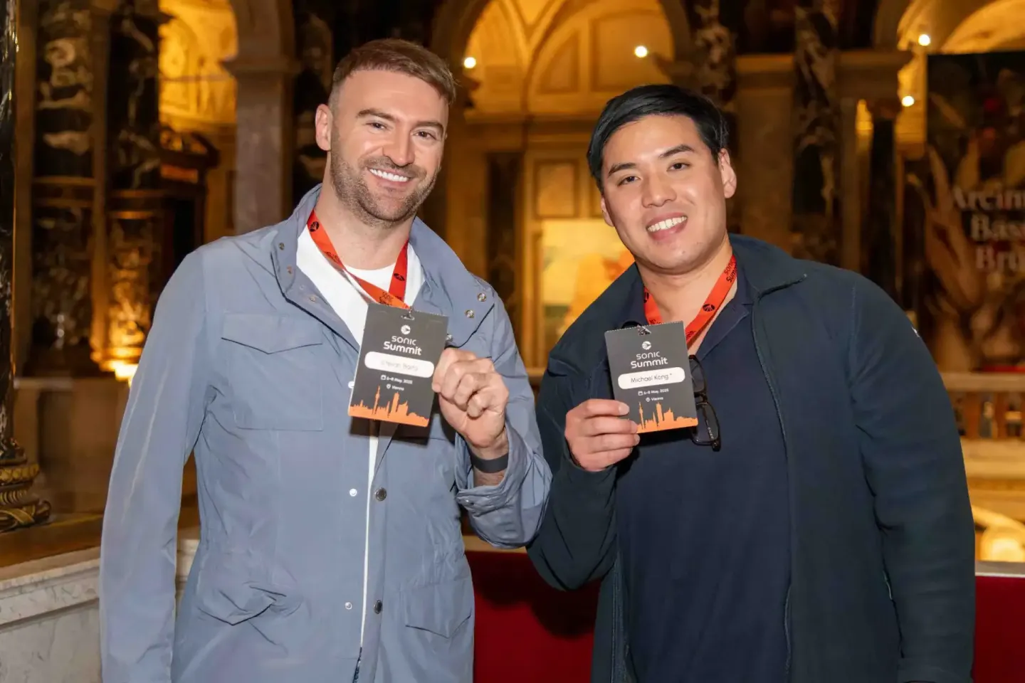 Zwei Teilnehmer mit Badges beim Sonic Summit Event in Wien, lächelnd vor historischer Kulisse