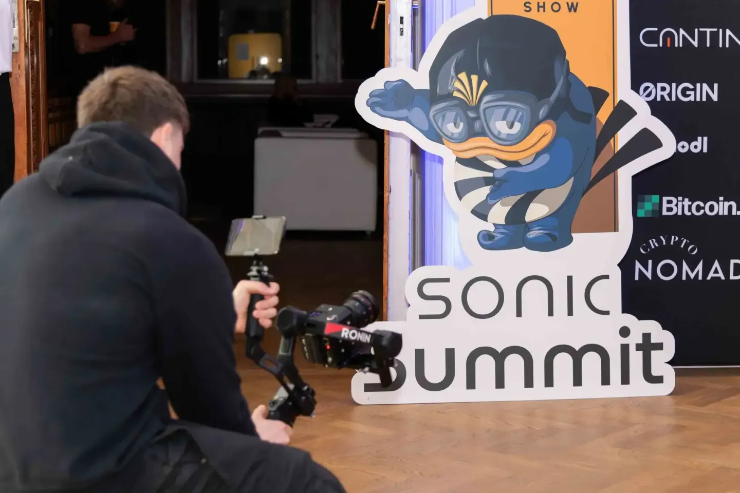 Eventfotograf dokumentiert Sonic Summit mit professioneller Kamera vor großem Branding-Aufsteller