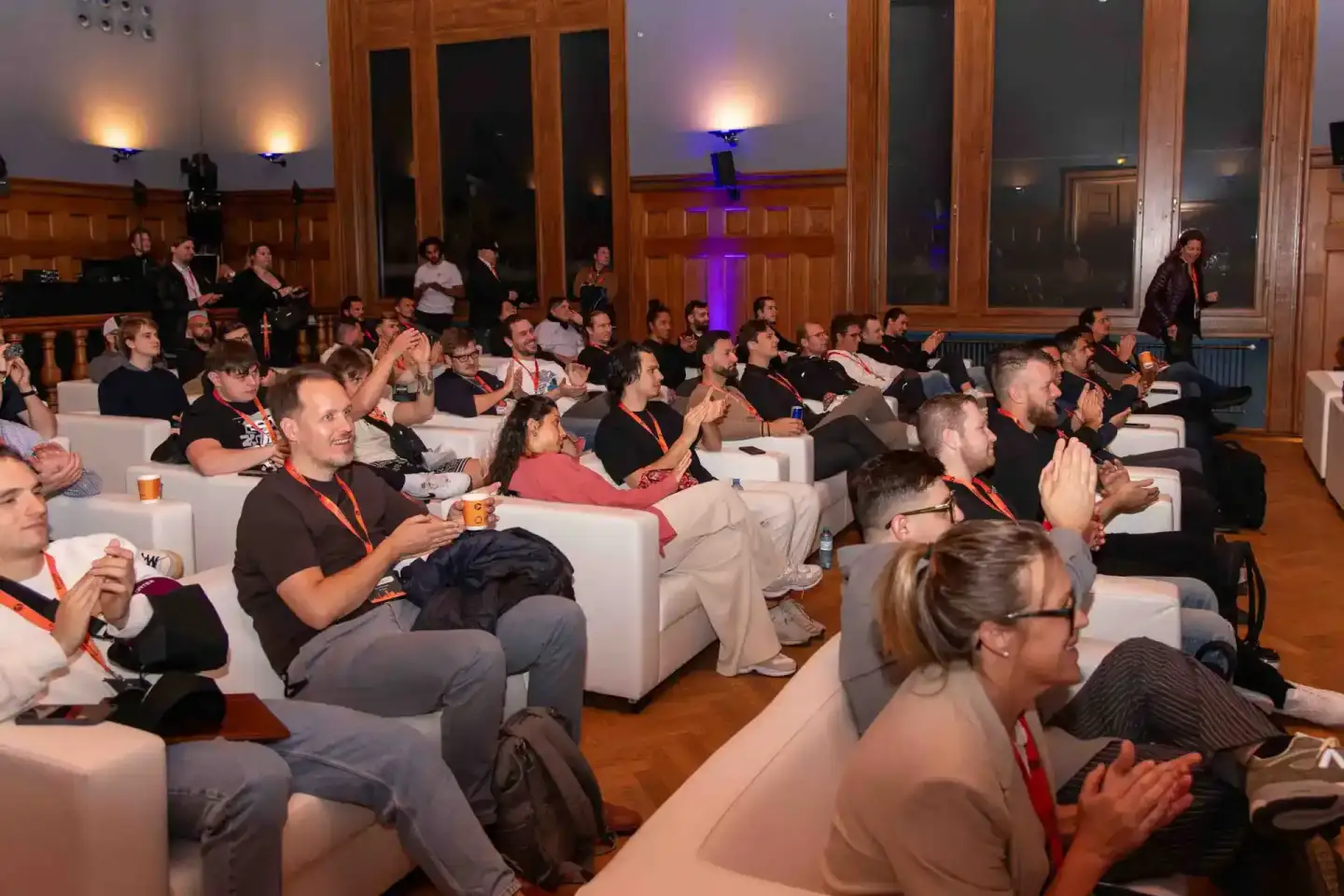 Publikum beim Sonic Summit in Wien sitzt auf weißen Sesseln und applaudiert während einer Veranstaltung mit beleuchteter Bühn