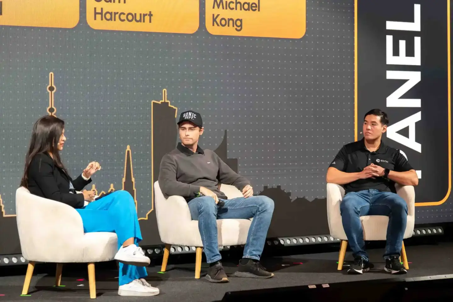 Drei Personen sitzen auf weißen Sesseln bei einer Podiumsdiskussion auf der Sonic Summit in Wien, im Hintergrund ist die skyl