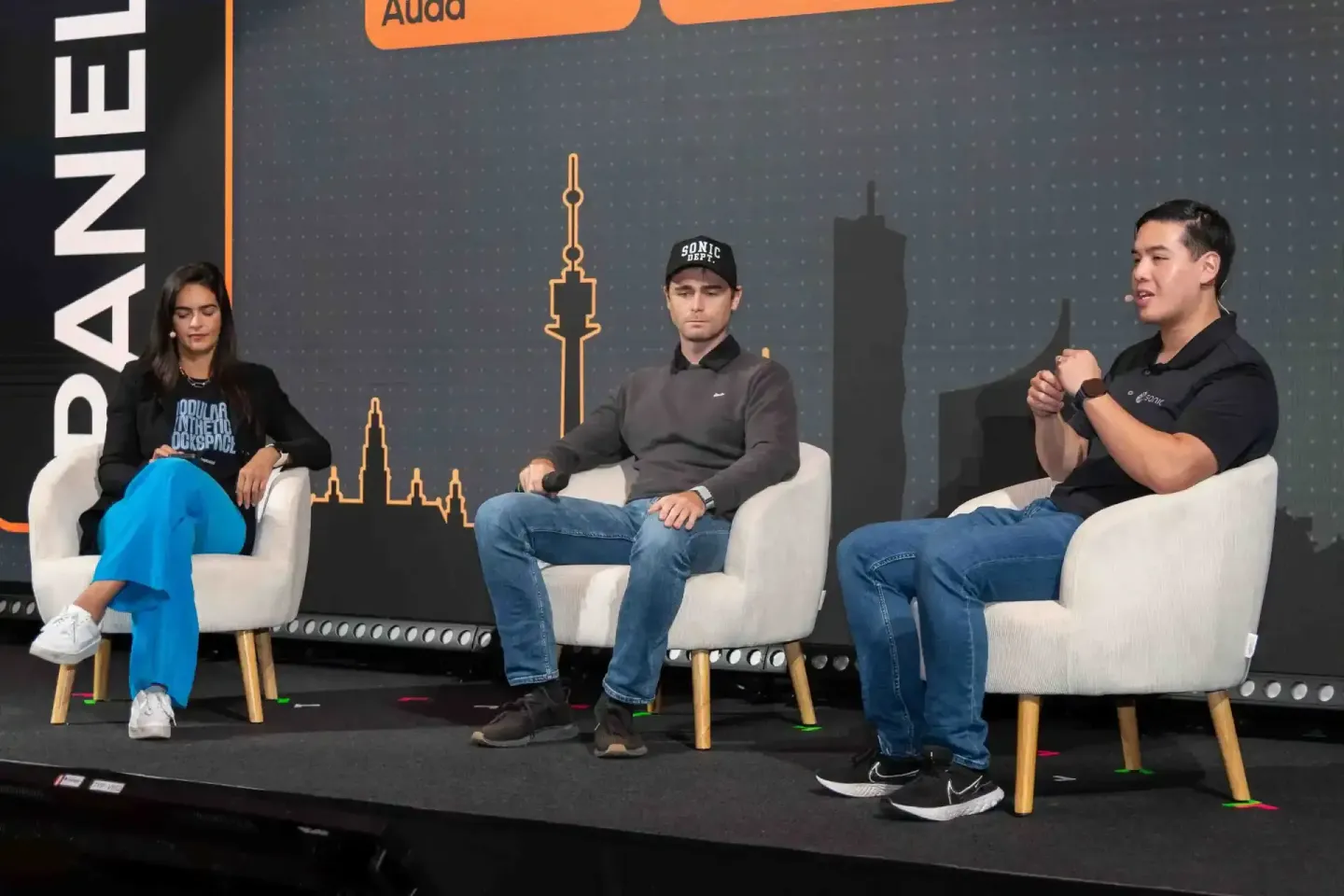 Drei Panelisten sitzen auf weißen Sesseln beim Sonic Summit Event Wien und diskutieren auf der Bühne mit Skyline-Grafik im Hi