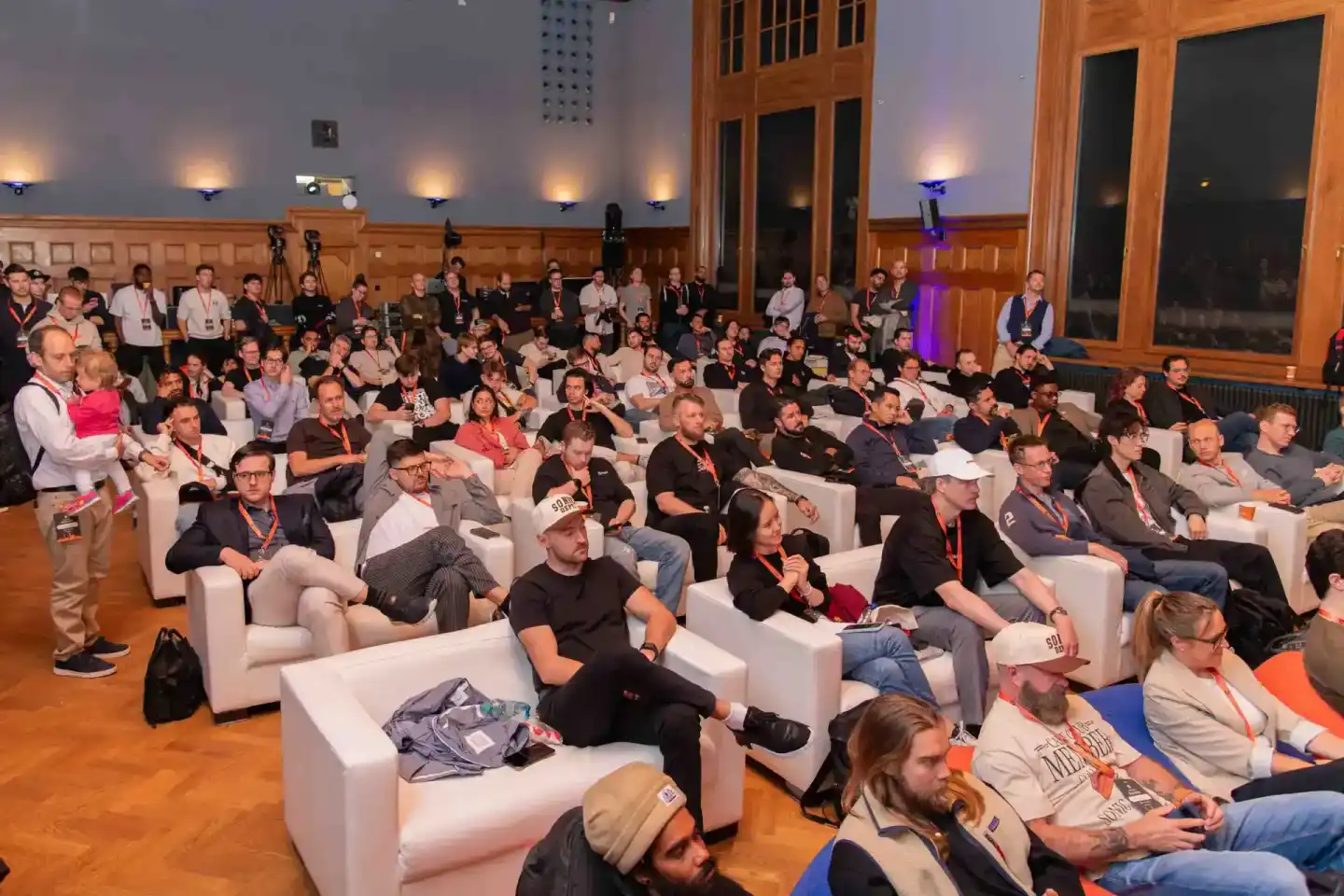 Großes Publikum sitzt auf weißen Sesseln in einem Holzsaal während einer Konferenz – professionelle Eventfotografie Wien