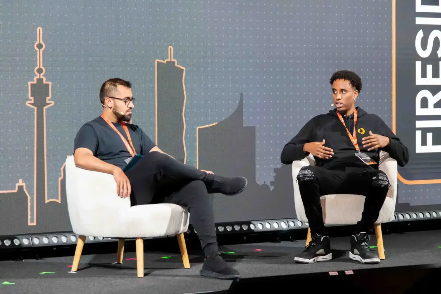 Zwei Sprecher auf der Sonic Summit Bühne in Wien sitzen in weißen Sesseln und diskutieren vor einer digitalen Skyline-Grafik 