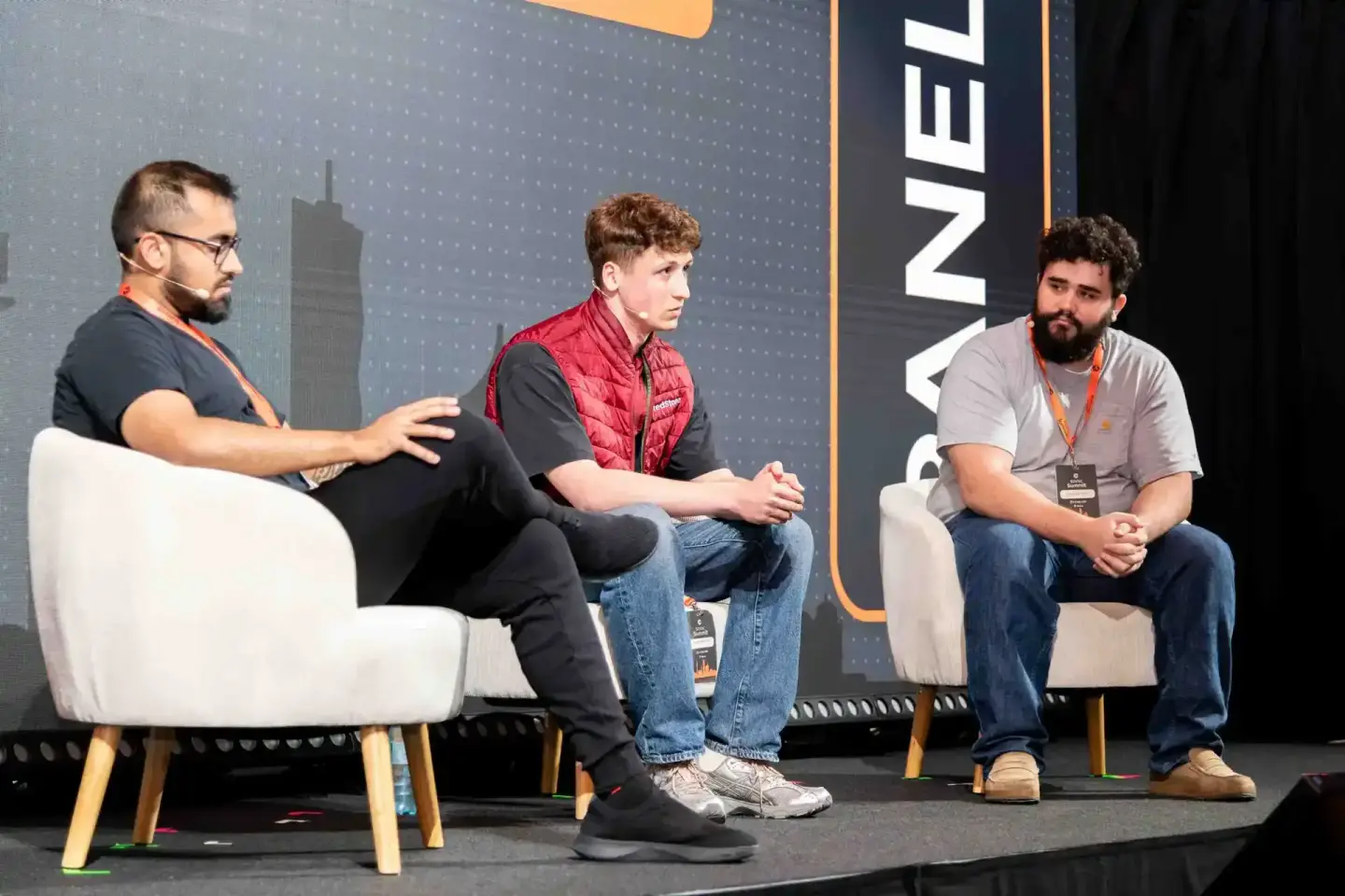 Drei Männer sitzen auf weißen Sesseln bei einer Podiumsdiskussion auf der Sonic Summit 2024 – professionelle Eventfotografie 