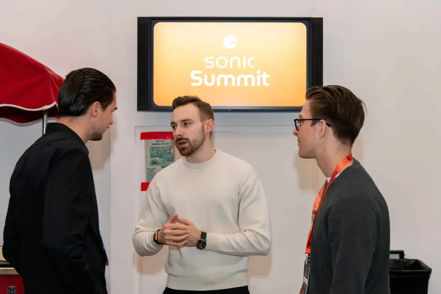 Drei Männer diskutieren beim Sonic Summit Event vor Monitor, Eventfotografie Wien dokumentiert Networking-Moment