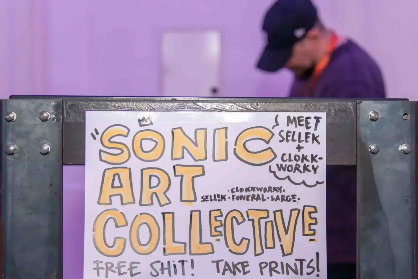 Sonic Art Collective Plakat bei Eventfotografie Wien – Veranstaltung mit lila Hintergrund und Person mit Cap