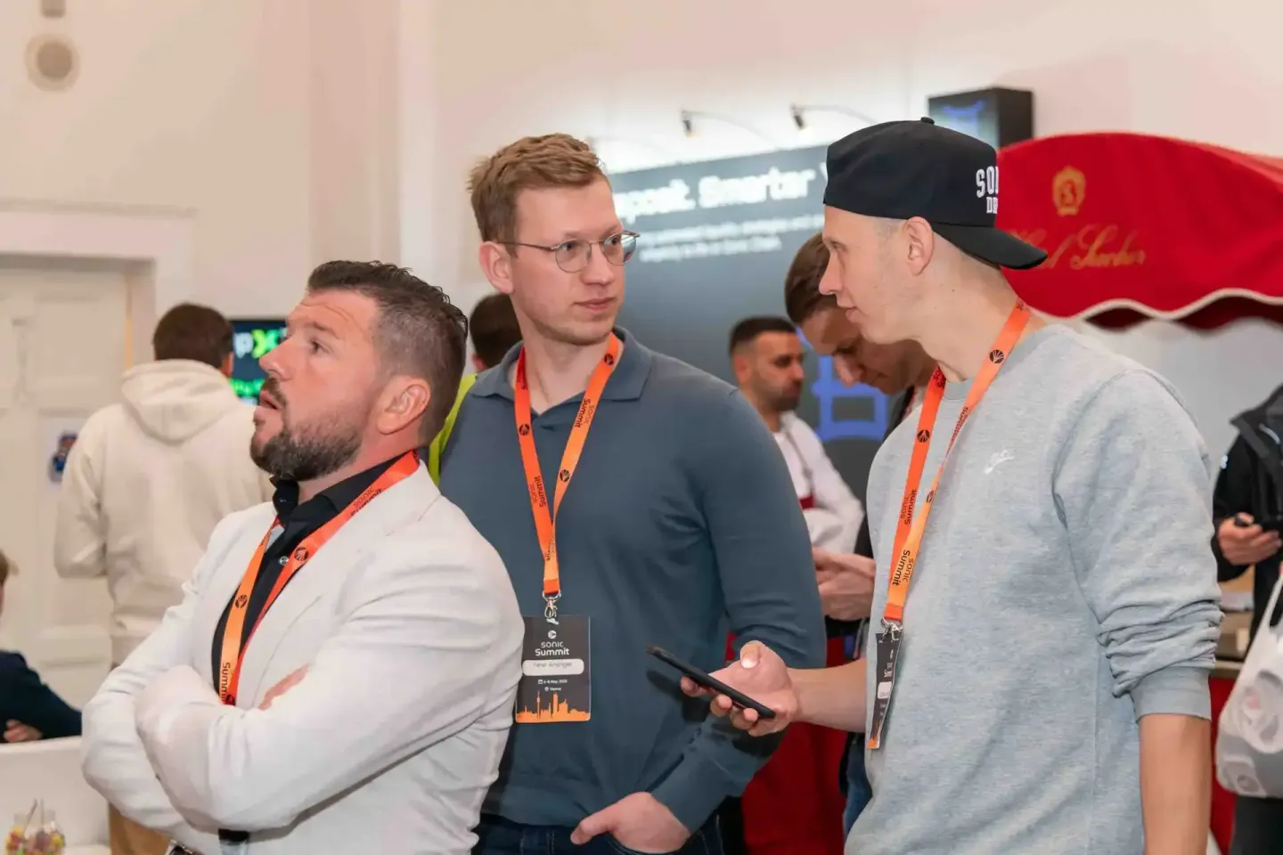 Drei Männer mit Lanyards diskutieren beim Sonic Summit Event, Eventfotograf dokumentiert Networking-Moment in Wien