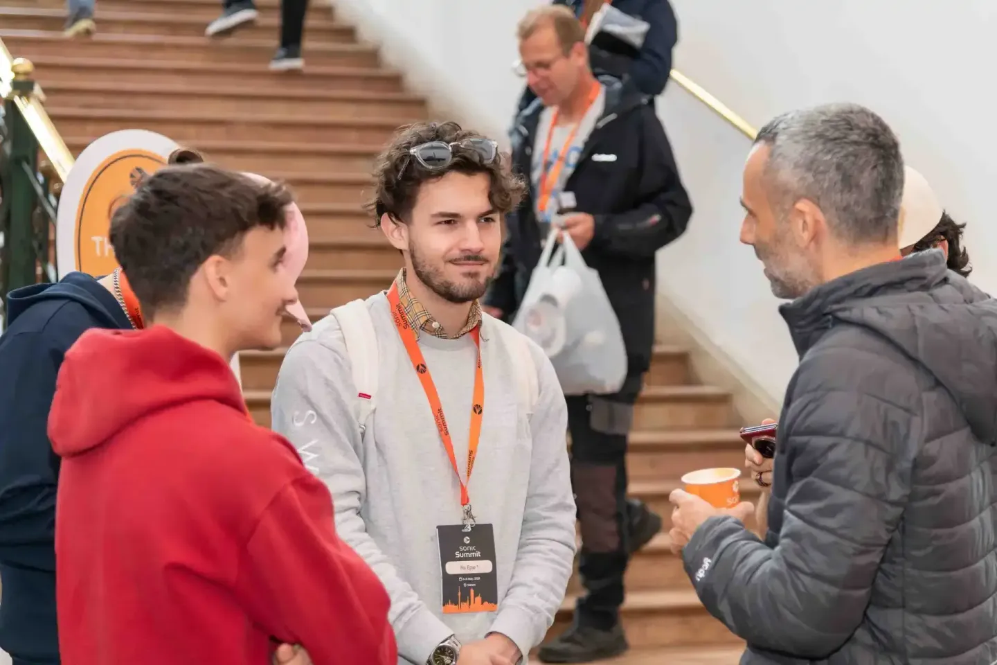 Eventfotograf dokumentiert Networking-Moment beim Sonic Summit: Drei Personen im Gespräch in einer modernen Treppenhalle, ein