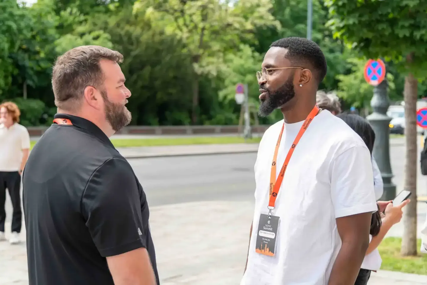 Zwei Männer im Gespräch auf dem Sonic Summit Event in Wien. Der Mann rechts trägt ein orange Lanyard und weißes T-Shirt. Even
