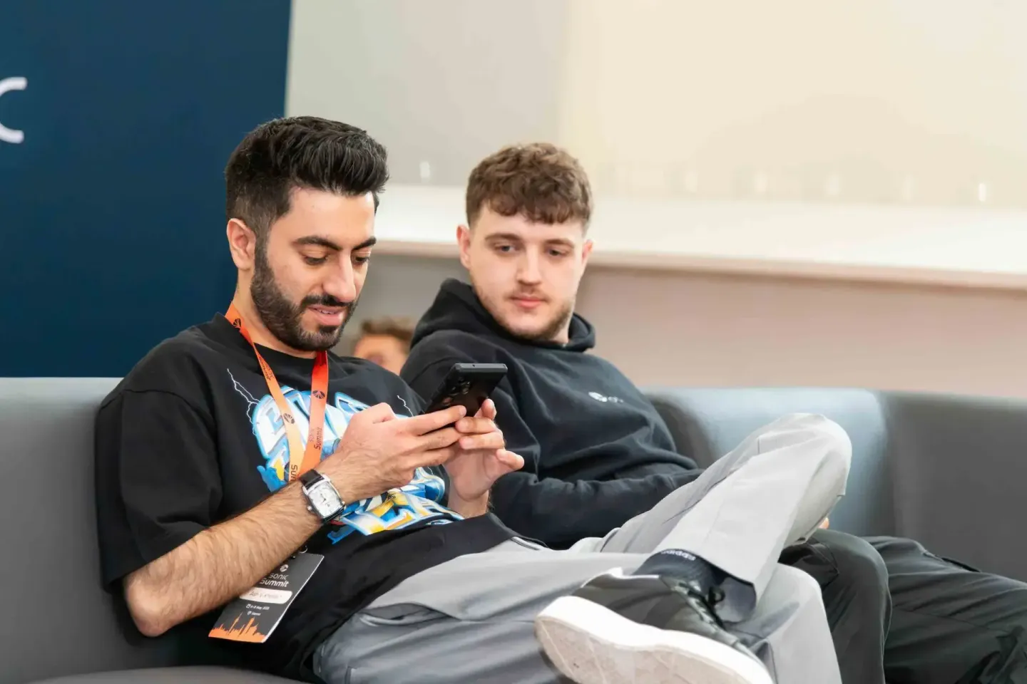 Zwei junge Männer sitzen auf einer Couch, einer hält ein Smartphone in der Hand. Eventfotograf dokumentiert die Sonic Summit 