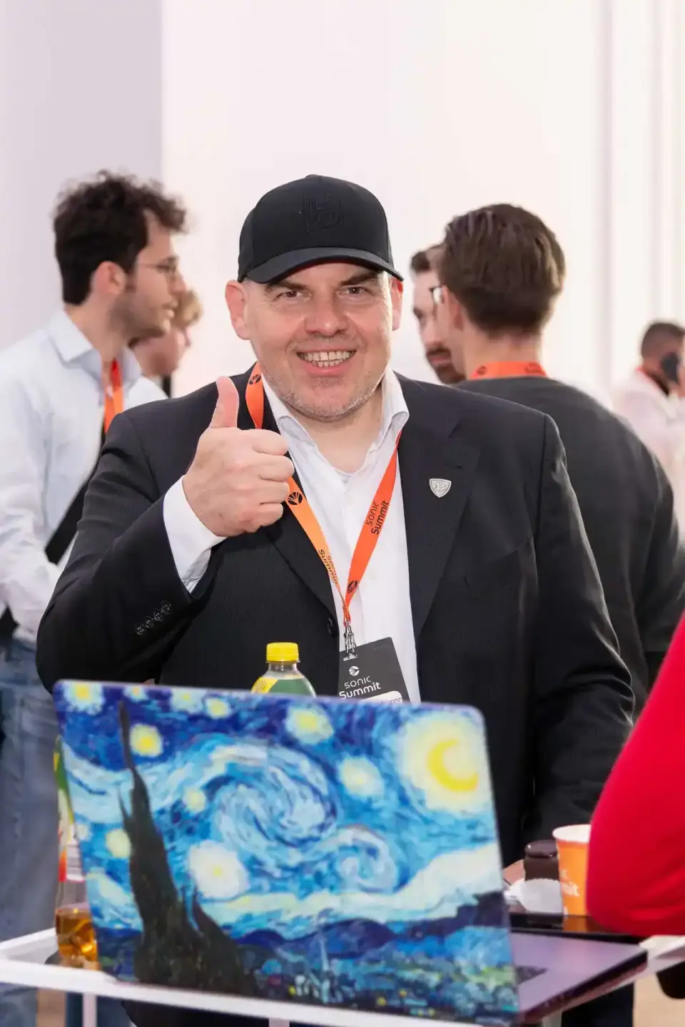 Lachender Mann im schwarzen Blazer und Cap mit Daumen hoch beim Sonic Summit Event - Eventfotografie Wien